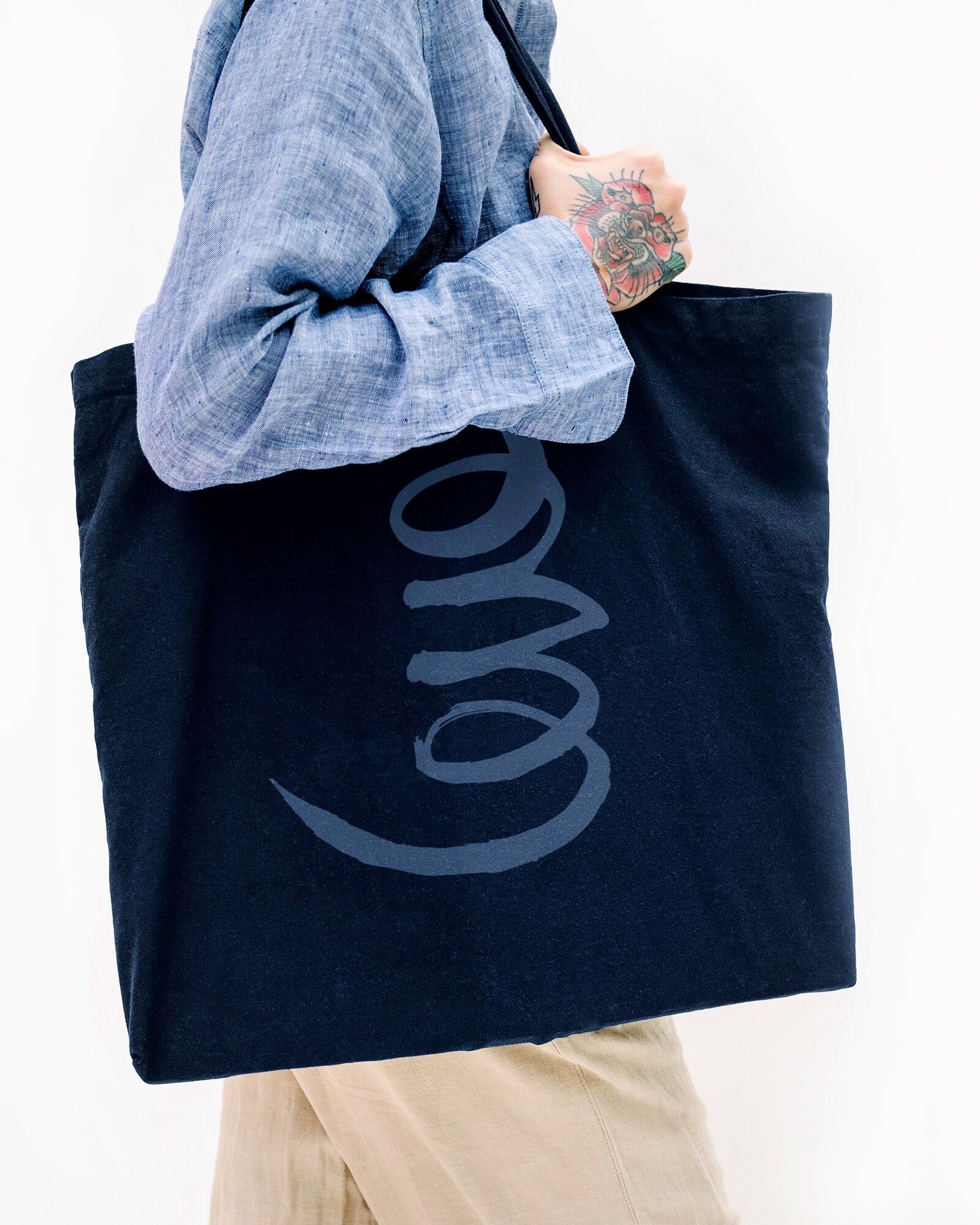 Tattooed Woman In A Blue Linen Shirt Holding A Black Tote Bag Mockup