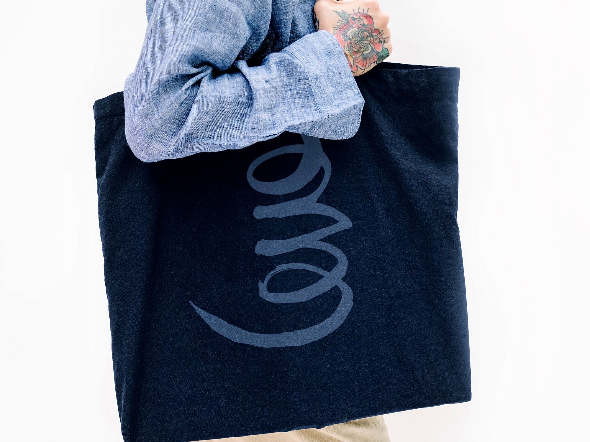 Tattooed Woman In A Blue Linen Shirt Holding A Black Tote Bag Mockup